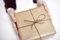 Woman holding gift wrapped in brown paper, decorated with string, close-up — Stock Photo