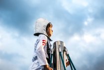 Портрет мальчика в костюме космонавта, смотрящего с вершины скалолазания на драматическое небо — стоковое фото