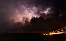 Lightning shoots up the updraft and anvil of tornadic supercell at night with car light trails — Stock Photo