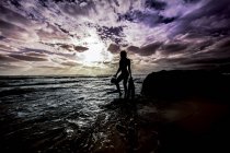 Silhouetted sexy woman standing on coastal rocks — Stock Photo