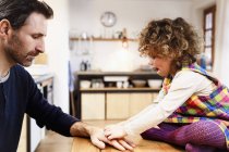 Girl on table sticking adhesive plaster onto father's hand — Stock Photo