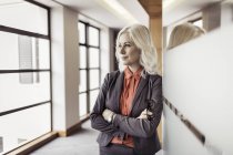 Портрет зрелой предпринимательницы со сложенными у дверей офиса руками — стоковое фото