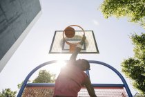 Young male basketball player throwing ball in sunlit basketball hoop — Stock Photo