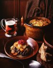 Estofado de venado con col roja, patatas en rodajas, zanahorias, cebollas y puerros con un vaso de cerveza y pan integral - foto de stock