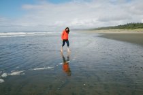 Mujer joven caminando descalza en la playa, Long Beach, Vancouver Island, Columbia Británica, Canadá - foto de stock