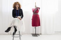 Woman sitting on stool by tailors dummy looking at camera — Stock Photo