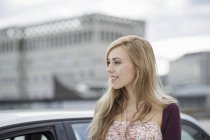 Langhaarige blonde junge Frau wartet mit Auto in der Stadt — Stockfoto