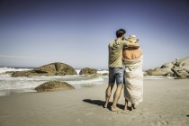 Rear view of couple wrapped in blanket looking out from beach, Cape Town, South Africa — Stock Photo