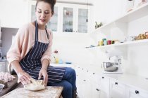 Young woman sitting on kitchen counter shaping dough — Stock Photo