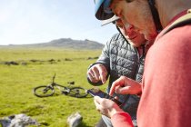 Велогонщики на склоне холма смотрят на смартфон — стоковое фото