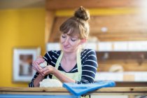 Mujer joven trabajando en panadería, rodando masa en las manos - foto de stock