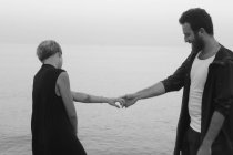 Молодая пара, стоящая у моря, держась за руки — стоковое фото