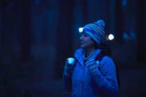 Caminhante feminina usando tocha na cabeça caminhando pela floresta à noite — Fotografia de Stock
