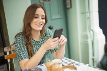 Frau im Straßencafé blickt lächelnd auf Smartphone — Stockfoto
