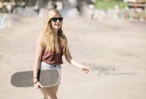 Young woman walking with skateboard in skatepark — Stock Photo