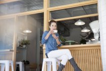 Jovem mulher sentada no bar no café, segurando xícara de café — Fotografia de Stock