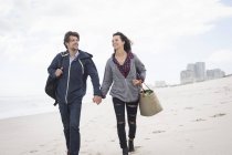 Romántica pareja joven paseando por la playa azotada por el viento, Western Cape, Sudáfrica - foto de stock
