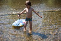 Boy ankle deep in water with body board — Stock Photo