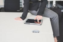 Waist down view of businesswoman sitting on office desk using digital tablet — Stock Photo