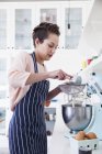 Молода жінка просіює борошно в миску для змішувача їжі на кухонній лічильнику — стокове фото