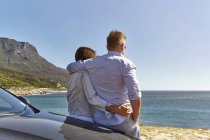 Пара опирается на капот автомобиля, смотрит на прибрежный вид, вид сзади, Кейптаун — стоковое фото