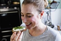 Femme adulte moyenne mangeant du pain de seigle en collation dans la cuisine — Photo de stock