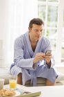 Reifer Mann auf Sofa liest Texte auf Handy und frühstückt — Stockfoto
