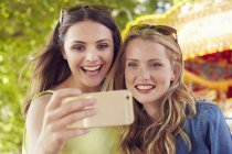 Mujeres tomando selfie, carrusel en el fondo - foto de stock