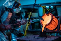 Male foundry workers pouring bronze melting pot in bronze foundry — Stock Photo