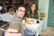 Пара в кафе на тротуаре разговаривает селфи — стоковое фото