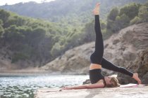 Junge Frau mit erhobenem Bein praktiziert Yogaposition auf Seebrücke, Mallorca, Spanien — Stockfoto