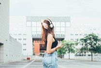 Молода жінка слухає навушники з рукою на голові поза офісною будівлею — стокове фото