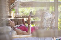 Junge Frau entspannt sich auf der Veranda beim Surfen mit digitalem Tablet — Stockfoto