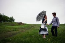 Пара стоящих в поле, держащихся за руки, молодая женщина, держащая зонтик — стоковое фото