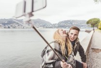 Young couple laughing taking smartphone selfie on harbour wall, Lake Como, Italy — Stock Photo