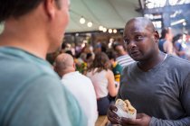 Clientes do sexo masculino conversando e comendo hambúrgueres no mercado cooperativo de alimentos stall — Fotografia de Stock