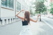 Rückansicht einer jungen Frau mit langen roten Haaren, die auf der Straße tanzt — Stockfoto