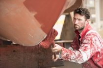 Male ship painter roller painting ship hull red in ship painters yard — Stock Photo