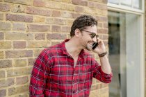 Junger Mann vor Ziegelmauer spricht auf Smartphone — Stockfoto