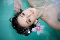 Bella giovane donna galleggiante nella piscina termale con orchidea viola — Foto stock