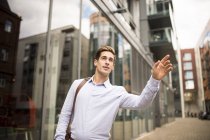 Young businessman hailing a cab outside office, London, UK — Stock Photo