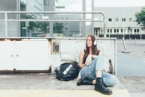 Молода жінка сидить за межами офісної будівлі, слухаючи навушники — стокове фото