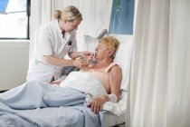 Медсестра допомагає пацієнту в лікарняному ліжку випити — стокове фото