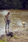Homme adulte moyen jouant avec le chien dans la rivière — Photo de stock