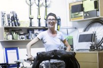 Женщина в мастерской держит лежачий велосипед, смотрит в камеру улыбаясь — стоковое фото