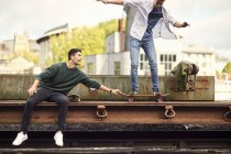 Two young men fooling around by train track, balancing on skateboard Bristol, UK — Stock Photo