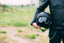 Середина чоловічої мотоциклістки, що стоїть на пустирі, тримає шолом — стокове фото