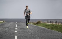 Male runner running along rural moorland road — Stock Photo