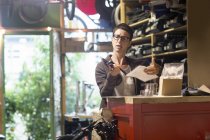 Femme au comptoir dans un atelier de vélo tenant la partie vélo et la paperasserie — Photo de stock