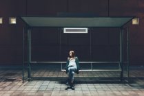 Молода жінка, що сидить на автобусній зупинці вночі — стокове фото